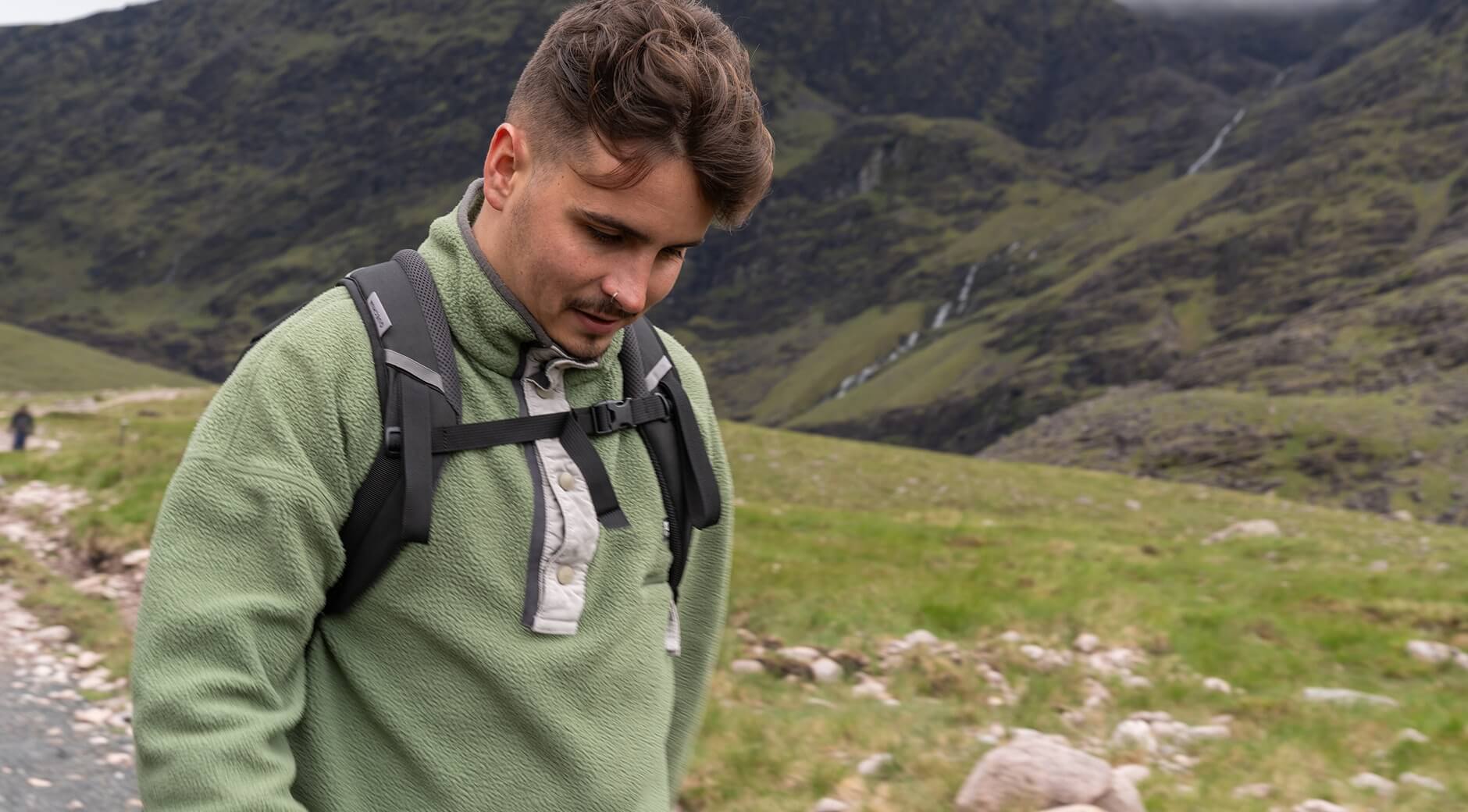 Man wearing a green fleece pullover with a backpack in the mountains.