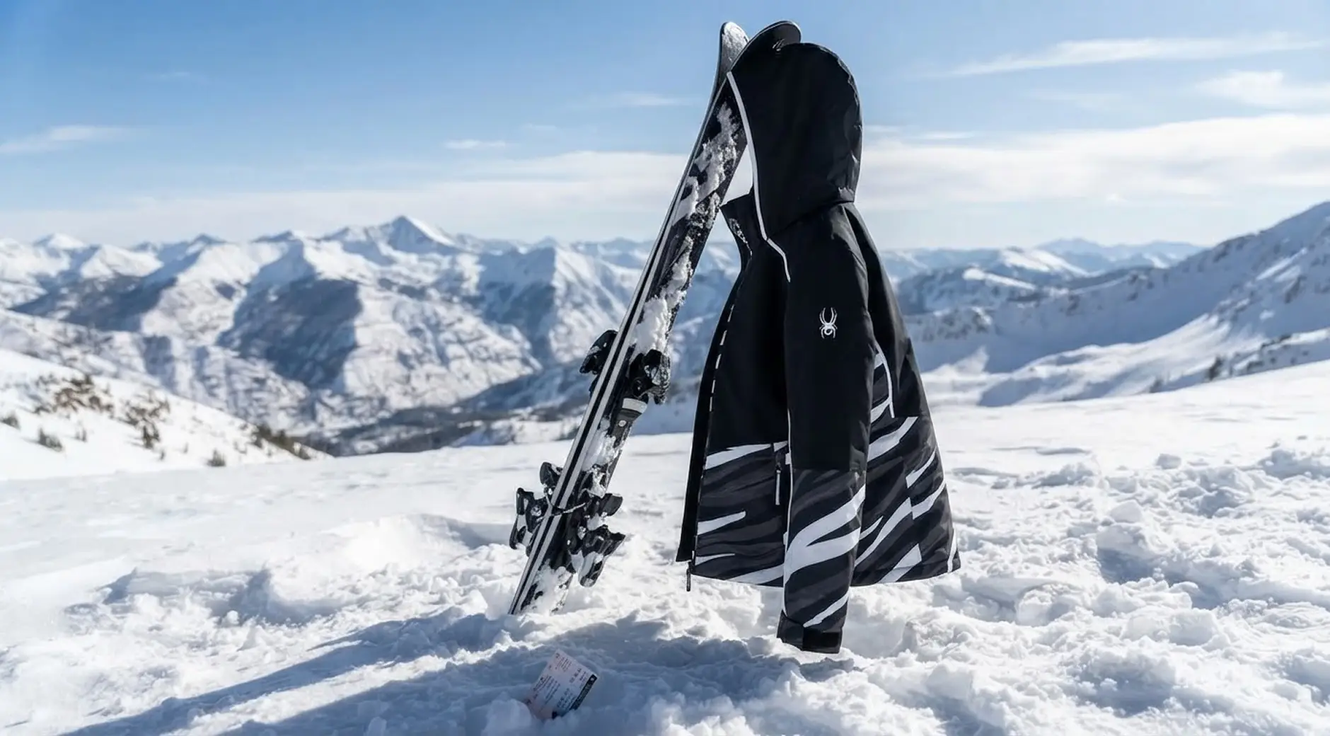 Black and white patterned ski jacket hanging on skis planted in snow