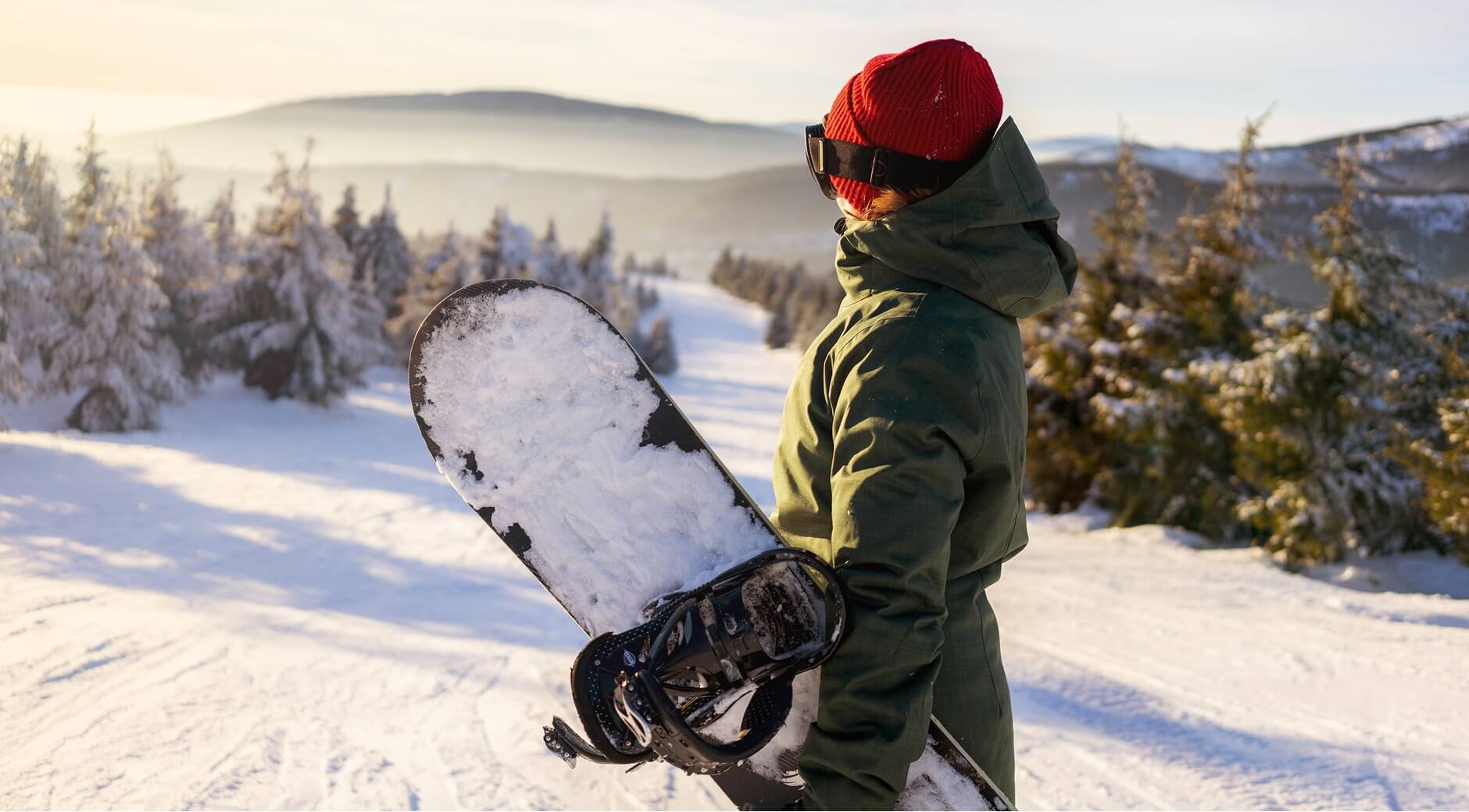 Snowboarder holding a board while looking out over a snowy slope.