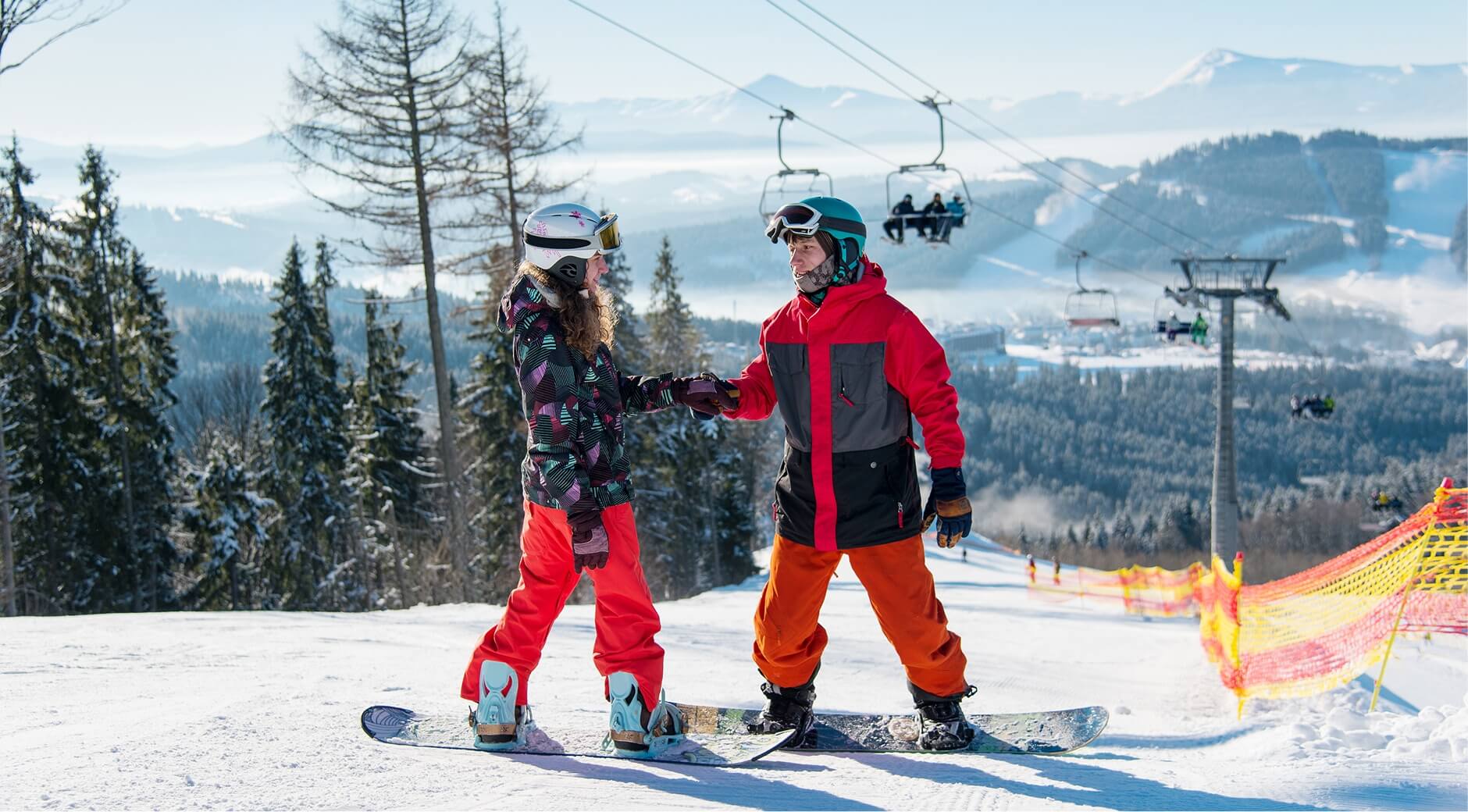 Two snowboarders in colorful jackets standing on a mountain slope.